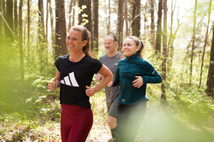 Tre av Midagons medarbetare tränar tillsammans i skogen. De joggar fram på ett stig och ler.