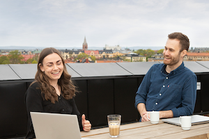 Två kollegor står vid ett ståbord på takterrassen på Midagons Örebrokontor. På bordet står kaffekoppar och en varsin dator.