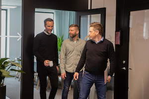 Tre kollegor på språng på Örebrokontoret. En har en kaffekopp i handen och en bär på sin dator.